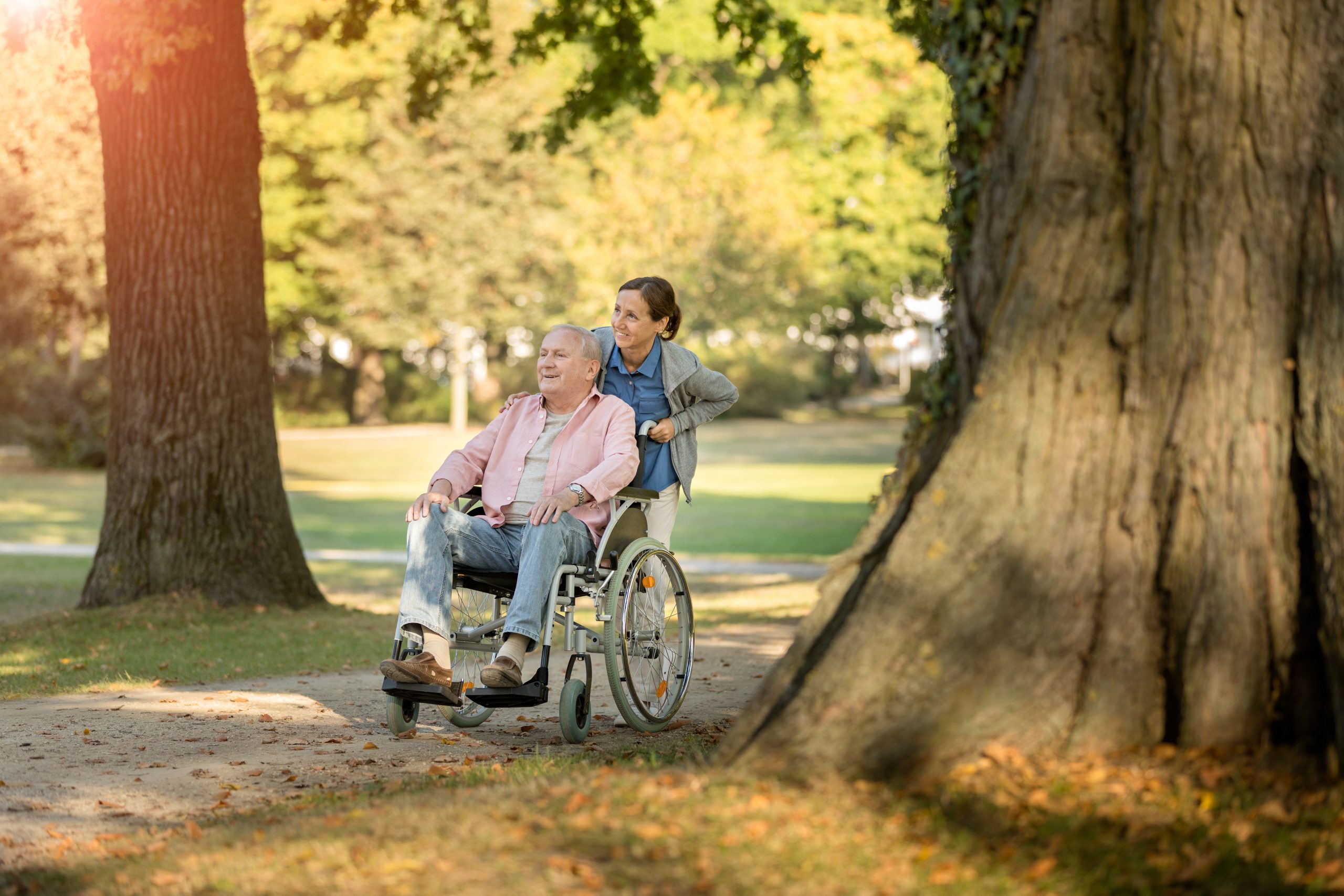 senior man in wheelchair with caregiver enjoying the outdoors