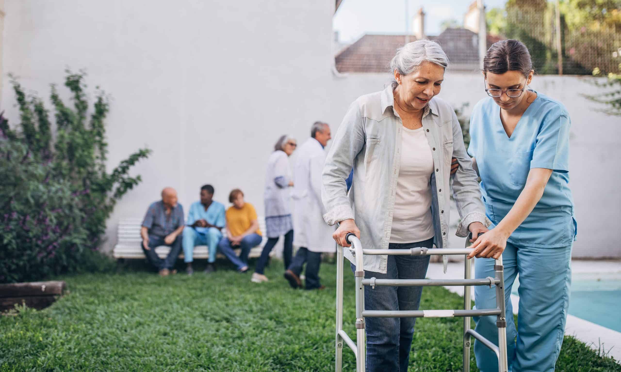 caregiver helping older woman use a walker outside